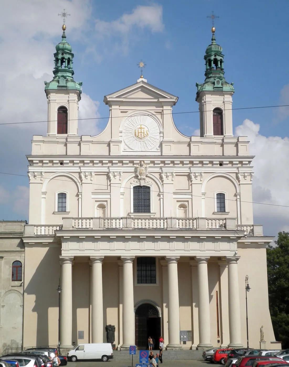 Barokowa archikatedra lubelska z kremowo-białą fasadą i dwiema wieżami zwieńczonymi zielonymi kopułami