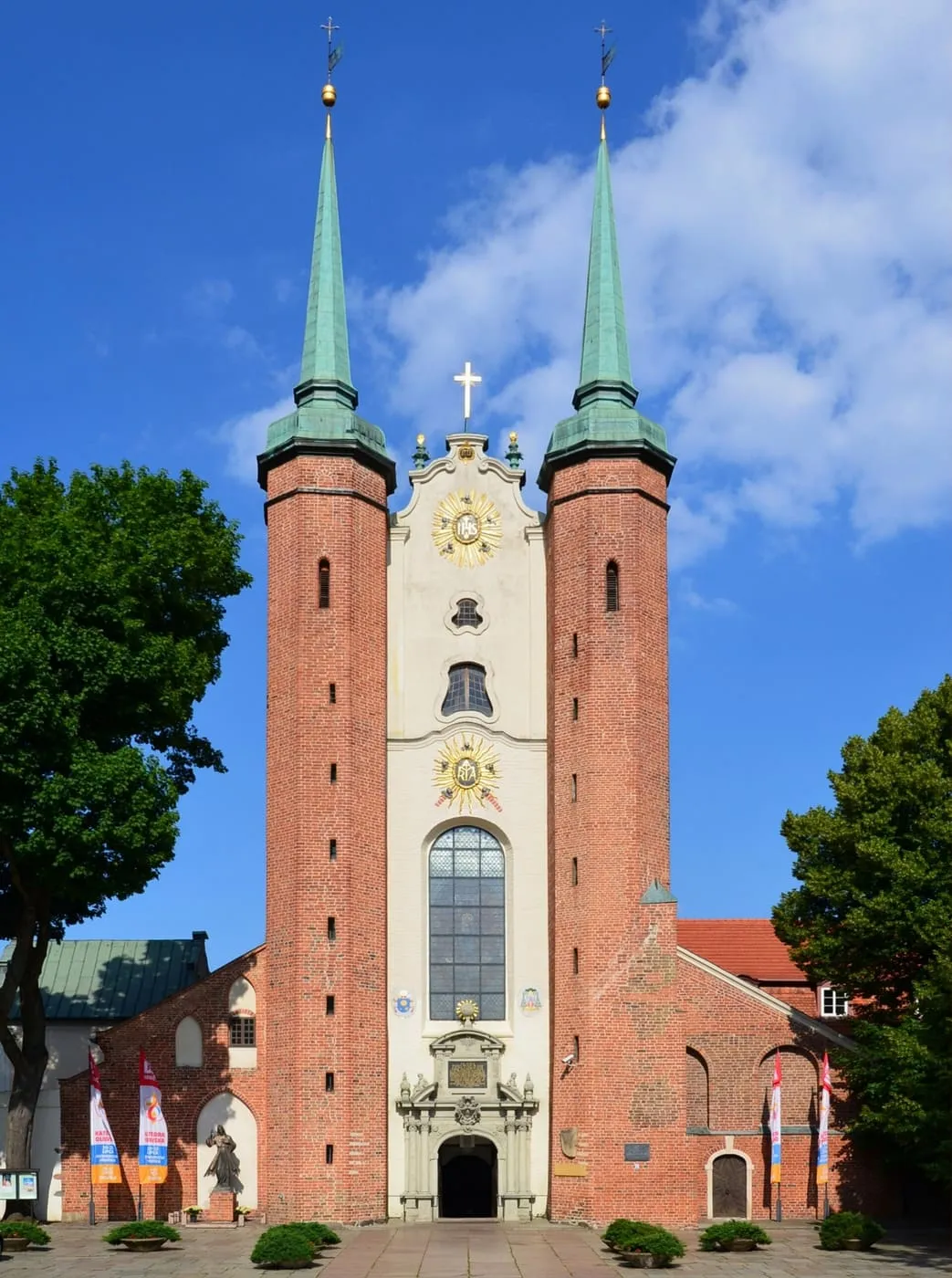 Archikatedra w Gdańsku-Oliwie z dwiema smukłymi ceglanymi wieżami flankującymi białą, barokową fasadę ze złoconymi symbolami