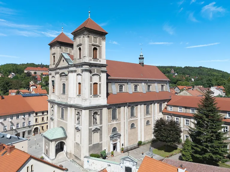 Bazylika Nawiedzenia Najświętszej Maryi Panny w Bardzie z lotu ptaka: dwuwieżowa fasada i nawa z czerwonymi dachami wśród zabudowy miasta i zalesionych wzgórz