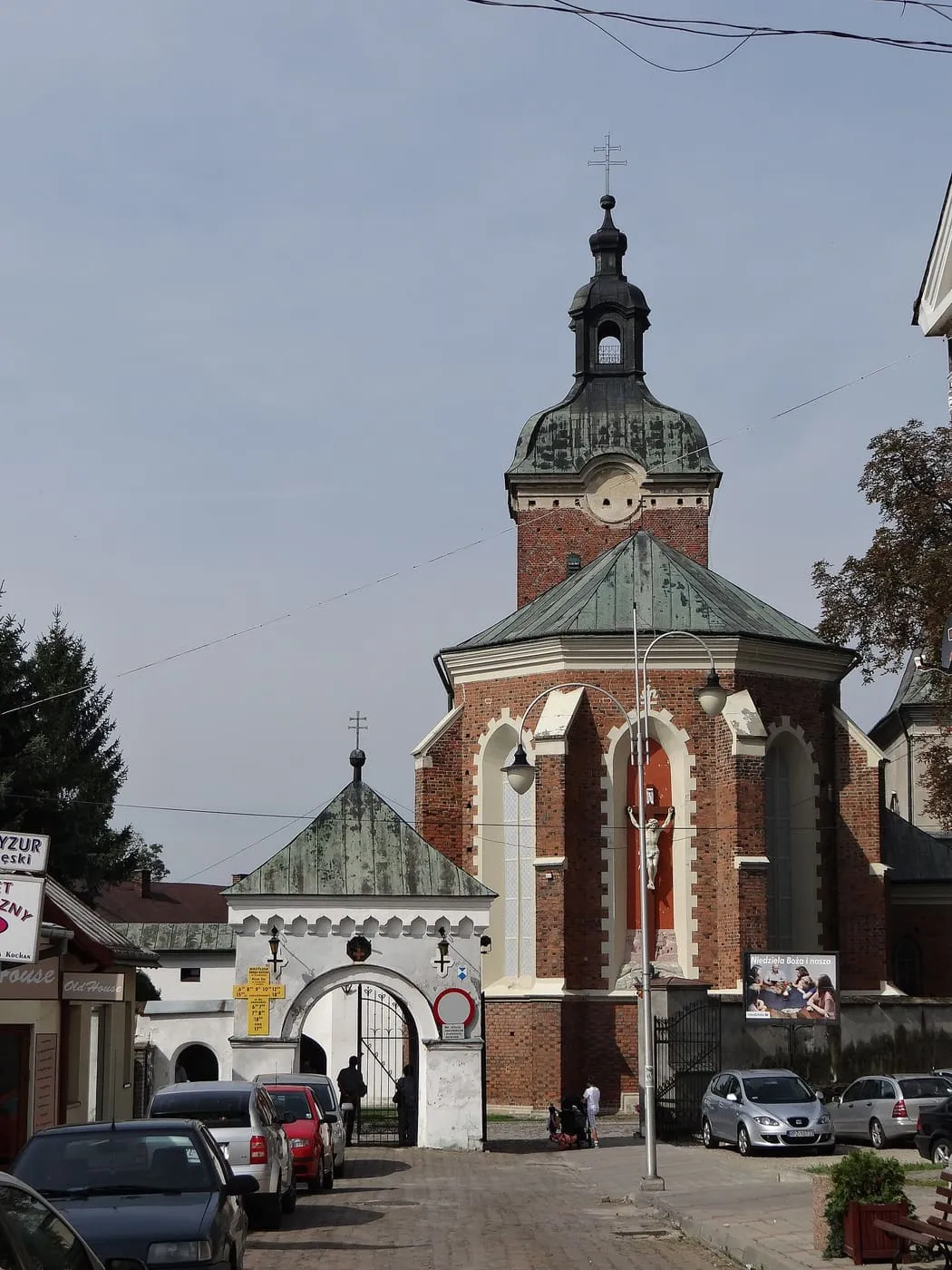 Ceglane, gotyckie prezbiterium bazyliki Ducha Świętego w Przeworsku z figurą Ukrzyżowanego we wnęce i wieżą z barokowym hełmem, obok bielonej bramy z arkadą