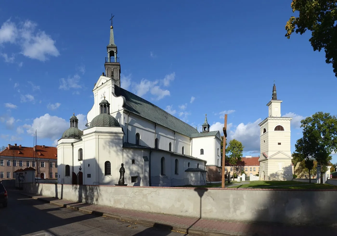 Biało-kremowa bazylika kolegiacka w Pułtusku z kopułą kaplicy i odrębną wieżą dzwonną, na tle błękitnego nieba z obłokami