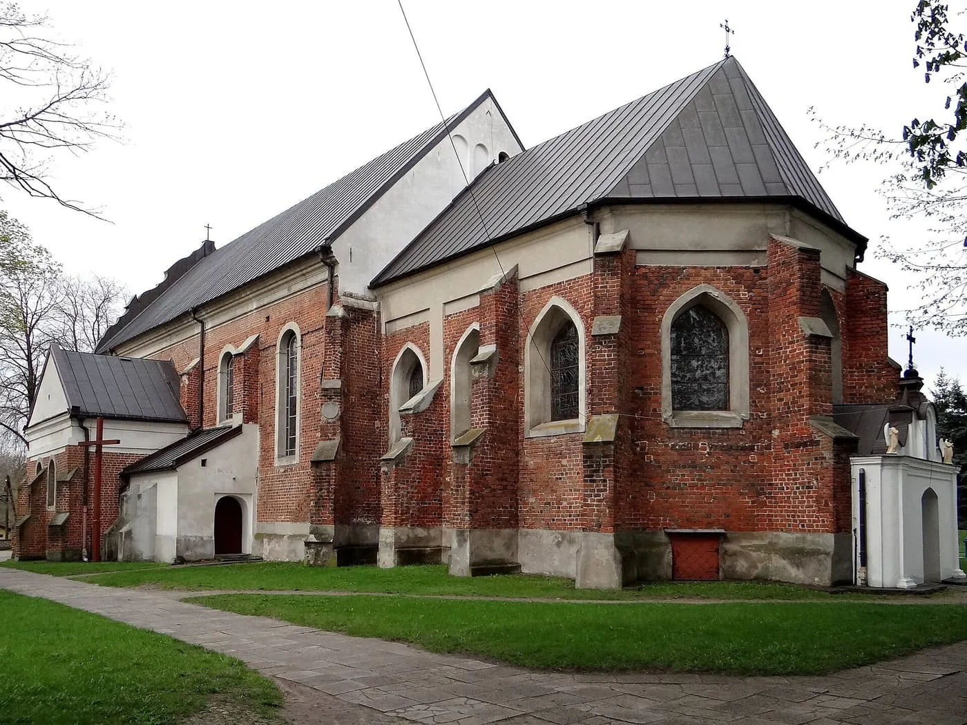 Ceglana apsyda bazyliki kolegiackiej w Uniejowie z wysoką, spiczastą wieżą, pod pochmurnym niebem