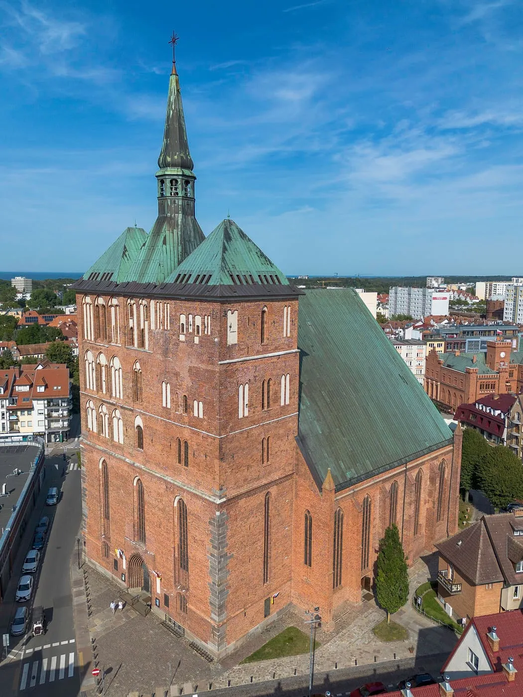 Ceglana, gotycka bazylika konkatedralna w Kołobrzegu z szeroką wieżą i zielonymi, miedzianymi dachami