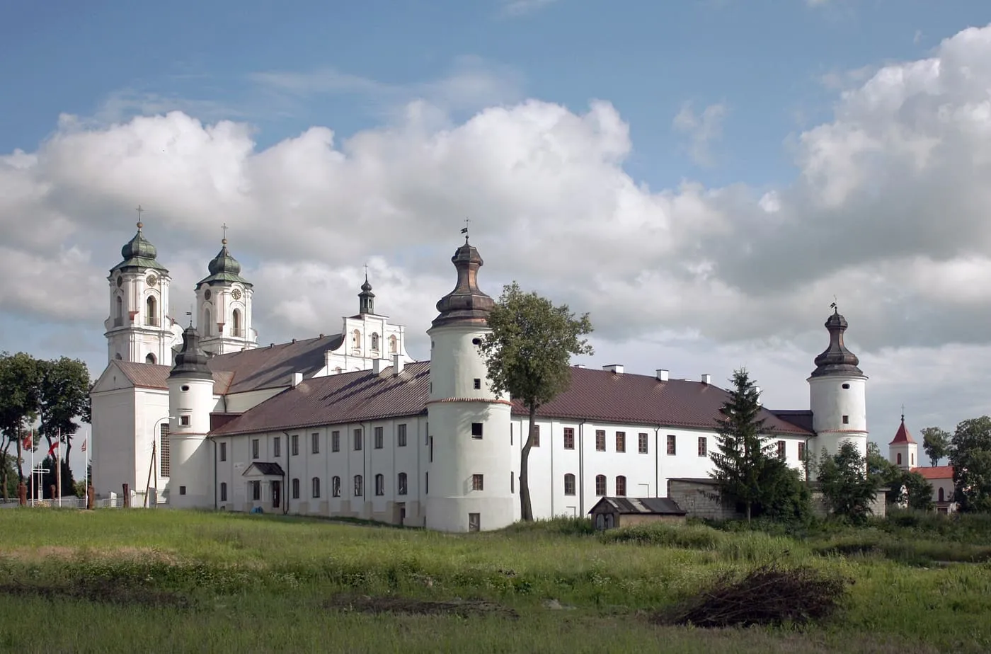 Biały, barokowy zespół klasztorny dominikanów w Sejnach z dwiema zielonymi kopułami kościoła i długim skrzydłem klasztornym