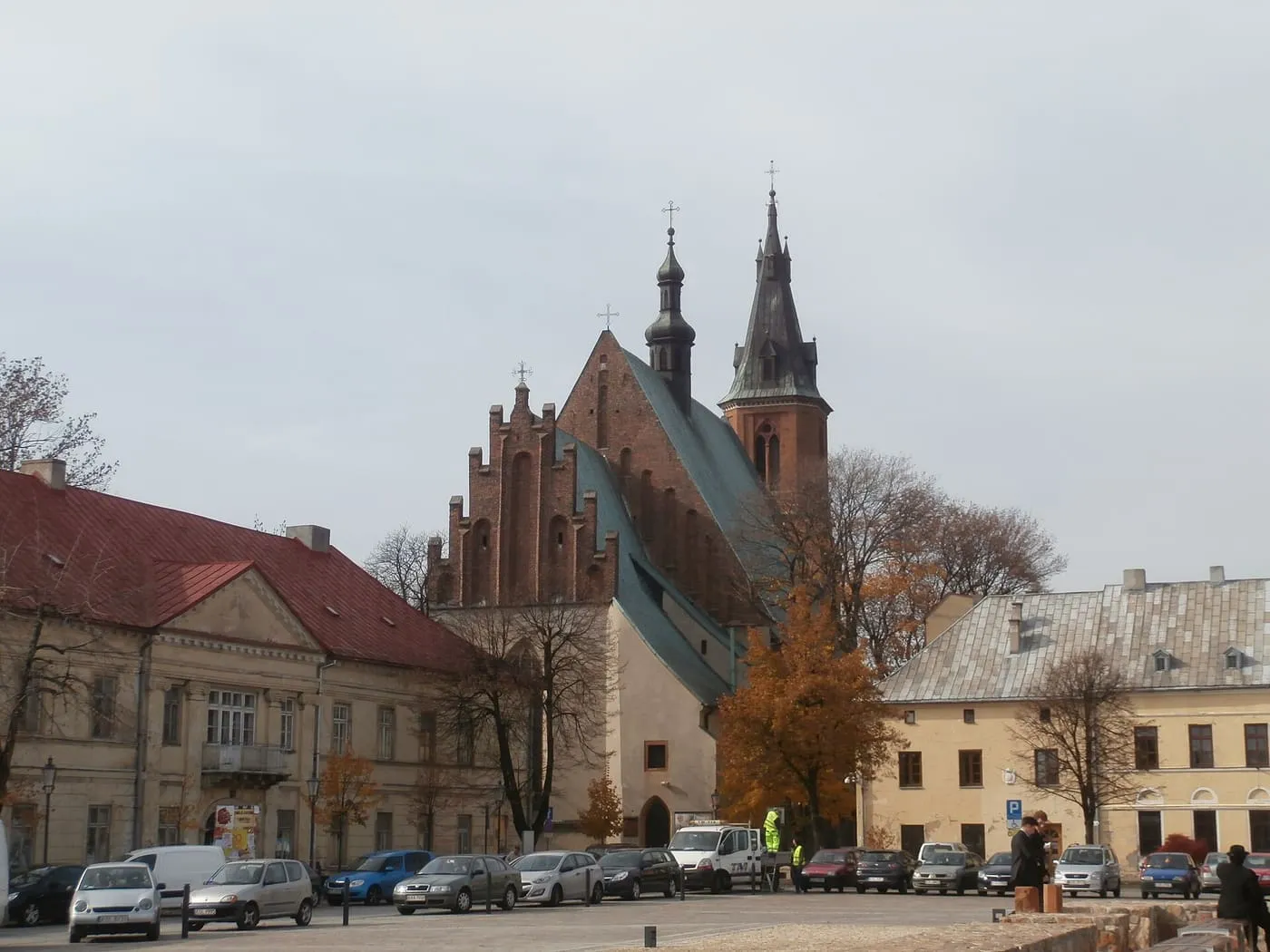 Gotycka bazylika św. Andrzeja w Olkuszu widziana z rynku, ze schodkowym ceglanym szczytem, zielonym dachem, sygnaturką i neogotycką dzwonnicą ze spiczastym hełmem, wśród jesiennych drzew