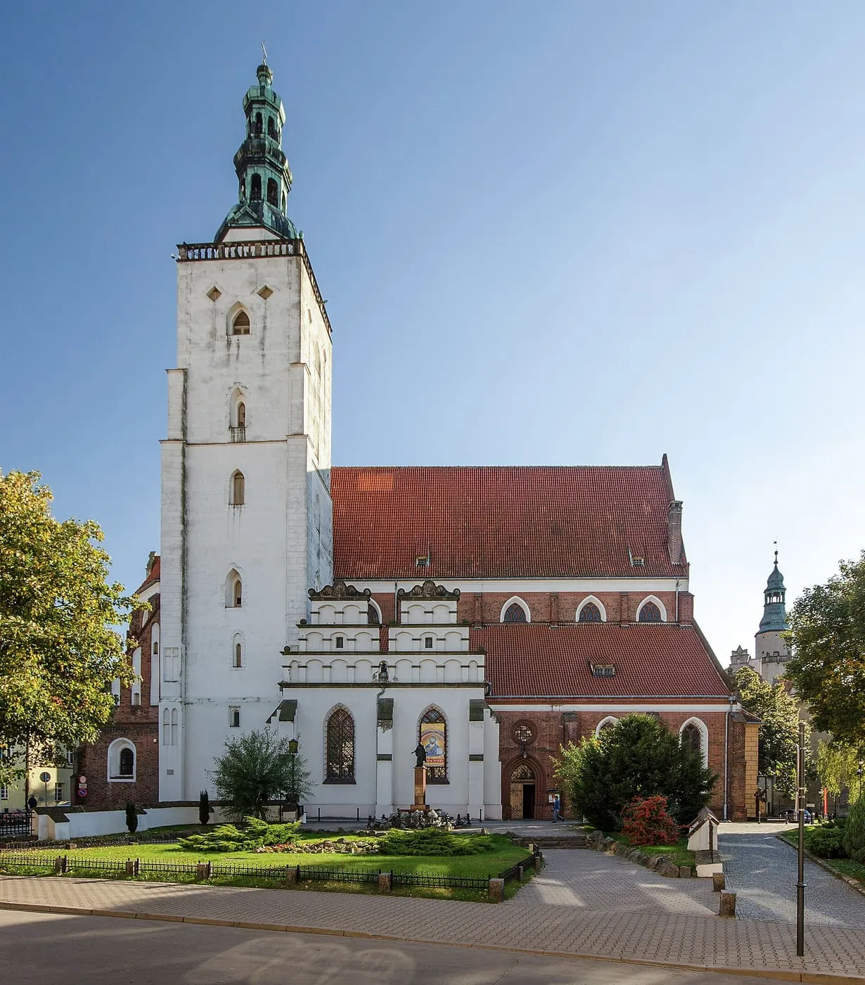 Biała wieża bazyliki św. Jana Apostoła w Oleśnicy z zieloną, barokową iglicą, nad czerwonym dachem nawy