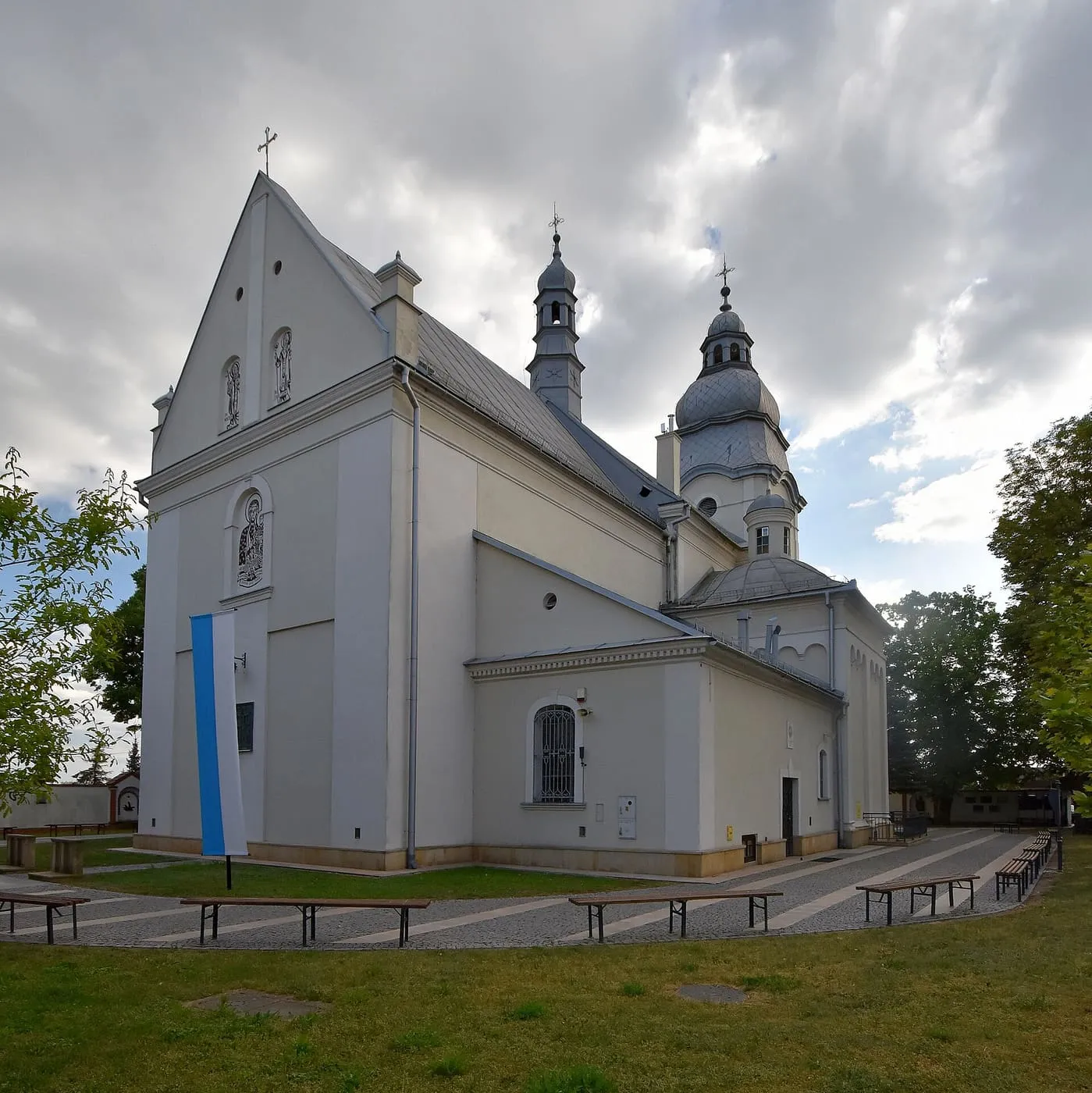 Jasna bazylika św. Mateusza w Mielcu z wysoką szczytową ścianą ozdobioną wizerunkami świętych, sygnaturką i wieżą z kopulastym hełmem, na tle zachmurzonego nieba