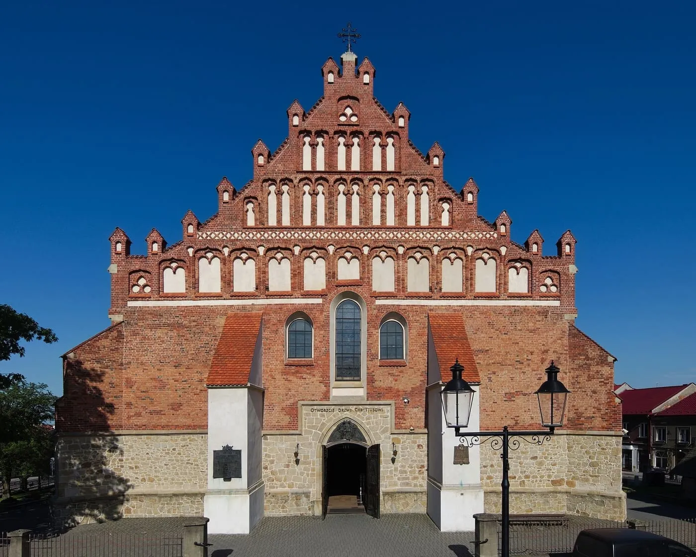 Późnogotycka fasada bazyliki św. Mikołaja w Bochni z bogatym, schodkowym szczytem ceglanym z białymi blendami i fryzem rombowym, nad kamiennym cokołem z portalem i napisem „Otwórzcie drzwi Chrystusowi”