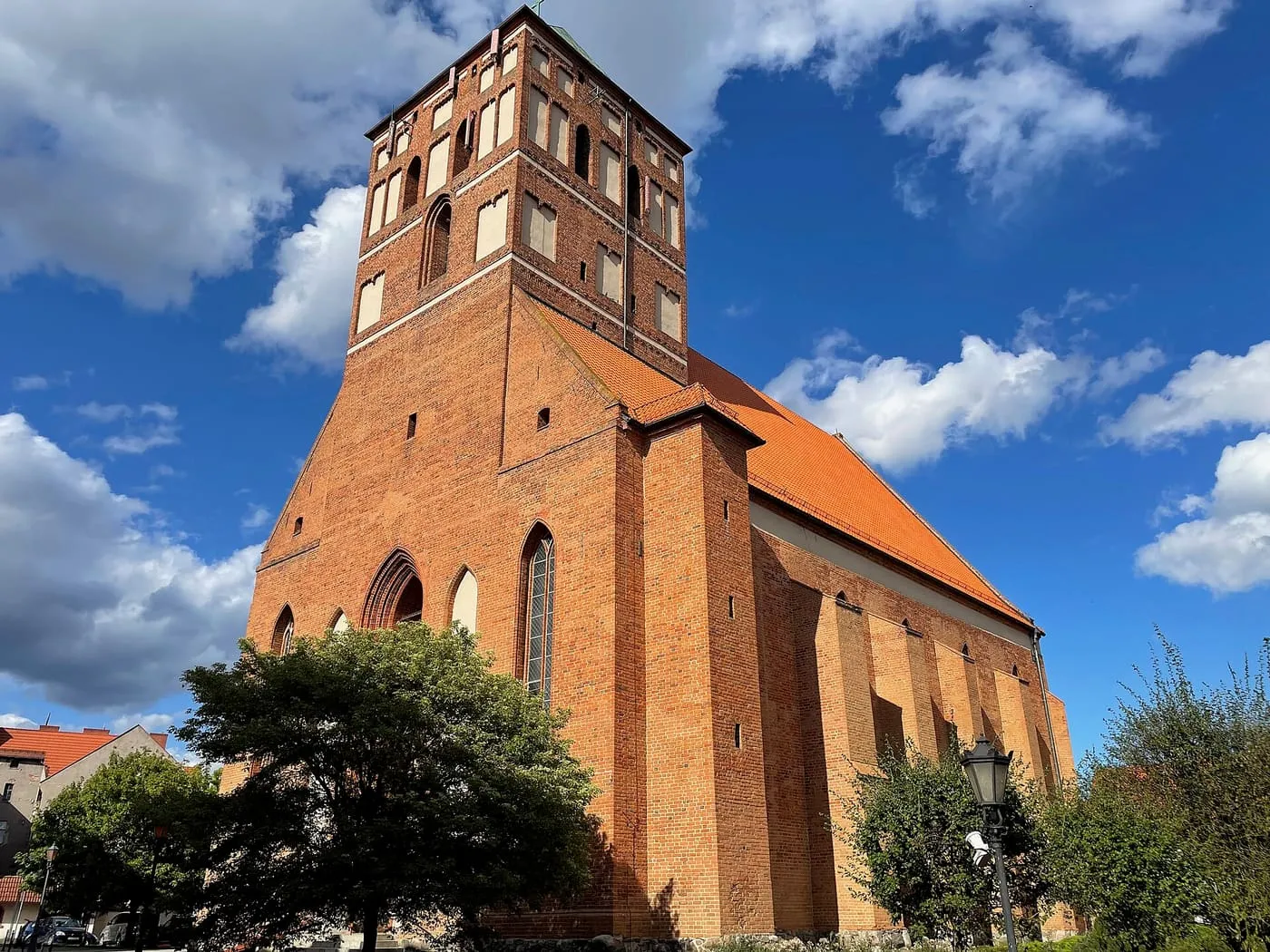 Gotycka, ceglana bazylika w Chojnicach z wysoką wieżą, sfotografowana pod kątem od dołu na tle błękitnego nieba z chmurami