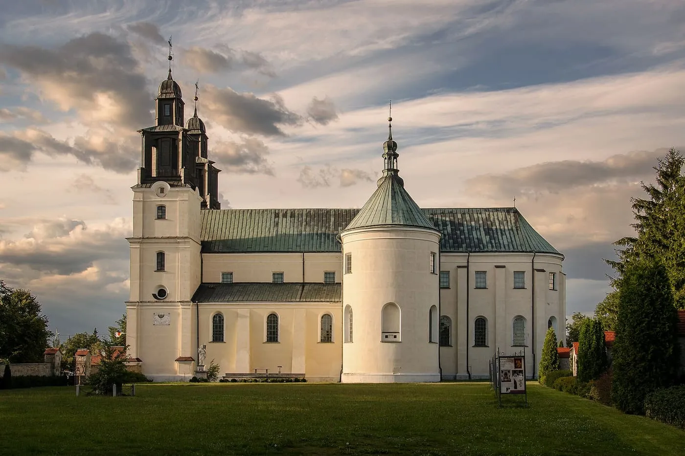 Biała bazylika w Gidlach z wysoką wieżą o ciemnym, wielokondygnacyjnym hełmie i cylindryczną przybudówką nakrytą stożkowym dachem z latarnią, w wieczornym świetle