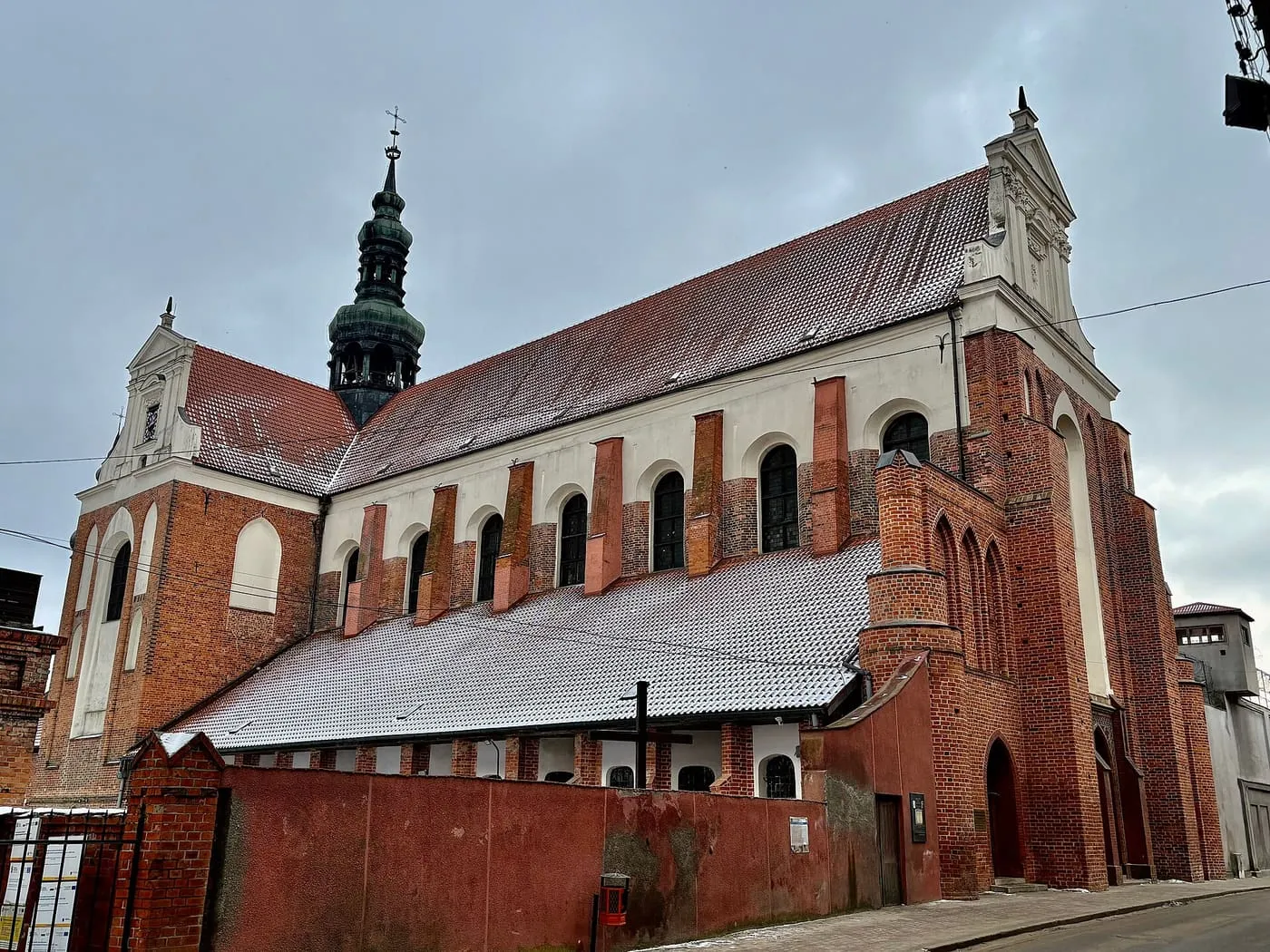 Ceglana, gotycko-barokowa bazylika w Koronowie z ciemną, cebulastą wieżą, ośnieżonym dachem zimą