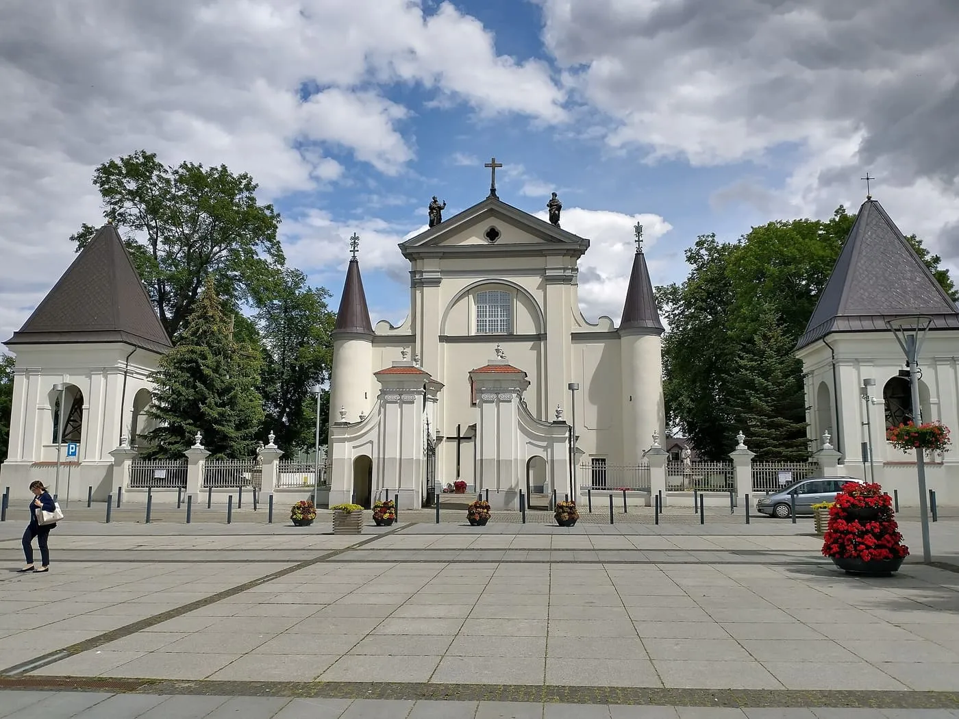 Jasna, barokowa fasada bazyliki w Węgrowie z figurami apostołów na szczycie i dwiema wieżyczkami o spiczastych hełmach, z bramą i dwiema czworobocznymi dzwonnicami po bokach placu
