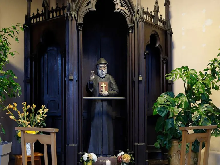 Figura św. Szarbela w kapturze zakonnym, z uniesioną dłonią w geście błogosławieństwa i księgą z krzyżem, w neogotyckiej kaplicy