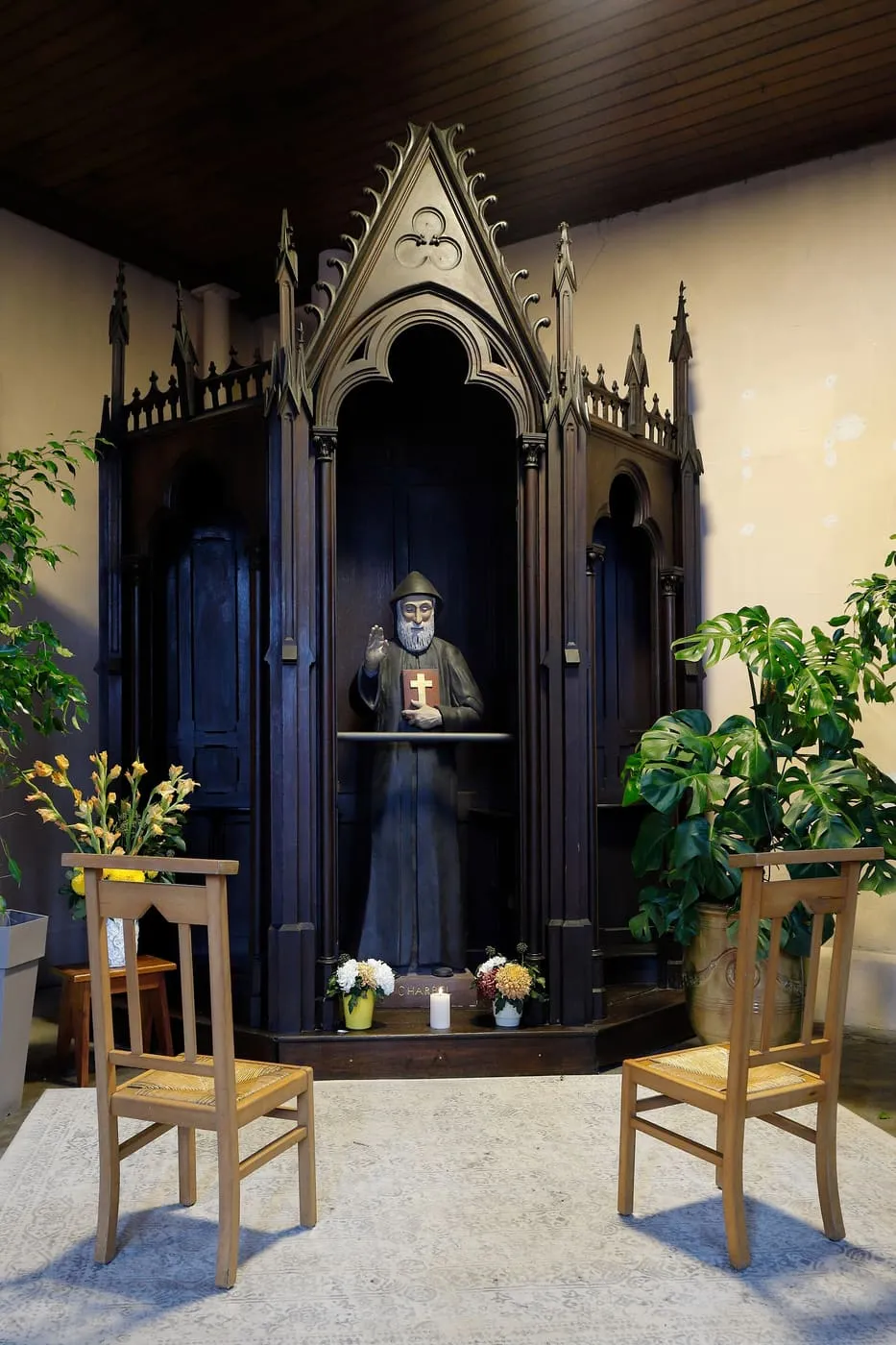 Figura św. Szarbela w kapturze zakonnym, z uniesioną dłonią w geście błogosławieństwa i księgą z krzyżem, w neogotyckiej kaplicy
