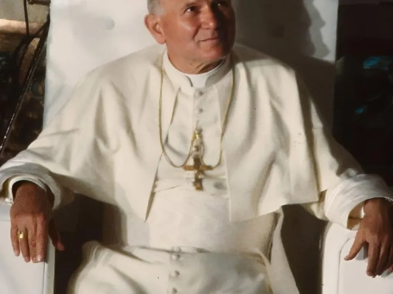Fotografia Jana Pawła II z 1983 roku: papież w białej sutannie z pektorałem siedzi w białym fotelu i spogląda w górę z lekkim uśmiechem, wykonana w Katowicach podczas pielgrzymki do Polski