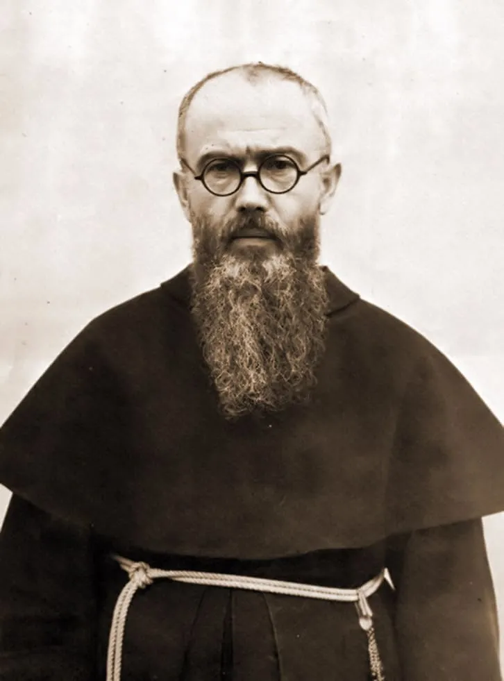 Czarno-biała fotografia o. Maksymiliana Kolbego z 1936 roku: franciszkanin w okrągłych okularach, z długą brodą, w ciemnym habicie przepasanym białym sznurem