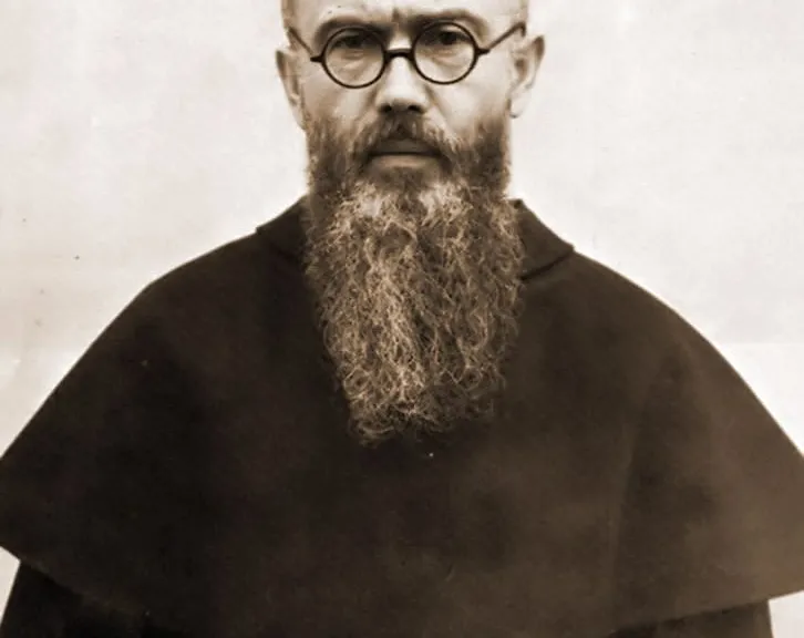 Czarno-biała fotografia o. Maksymiliana Kolbego z 1936 roku: franciszkanin w okrągłych okularach, z długą brodą, w ciemnym habicie przepasanym białym sznurem