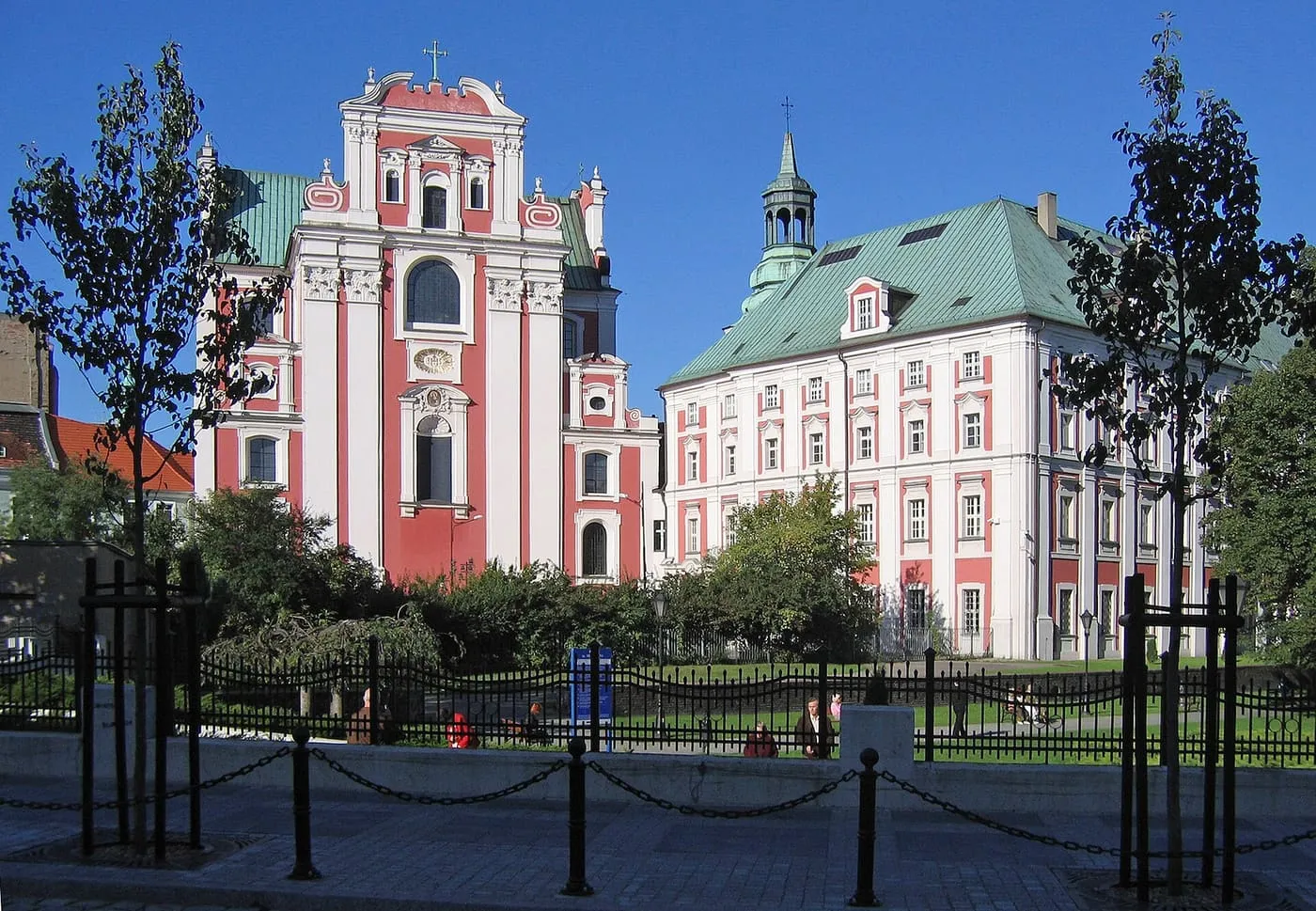 Różowo-biała, barokowa fasada Fary Poznańskiej obok zabudowań dawnego kolegium jezuickiego