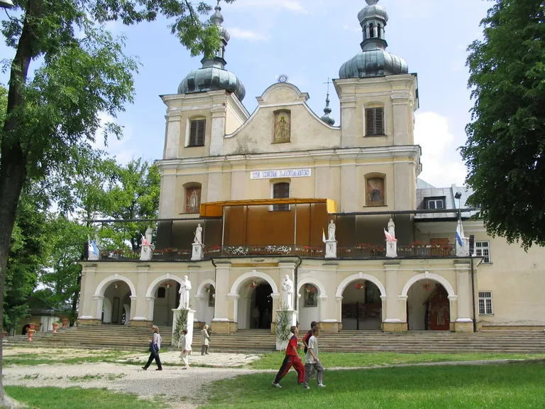 Kremowy, barokowy zespół klasztorny franciszkanów w Kalwarii Pacławskiej z dwiema ciemnymi kopułami i krużgankiem
