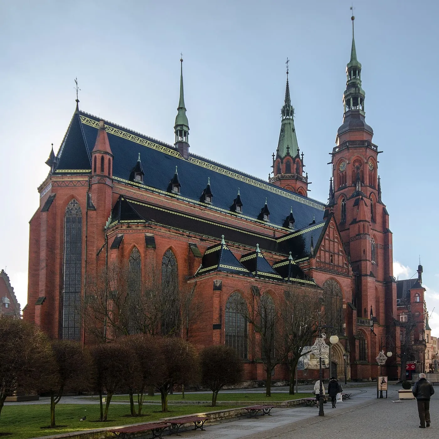 Katedra Świętych Apostołów Piotra i Pawła w Legnicy z ciemnym, spadzistym dachem i ceglaną wieżą zegarową