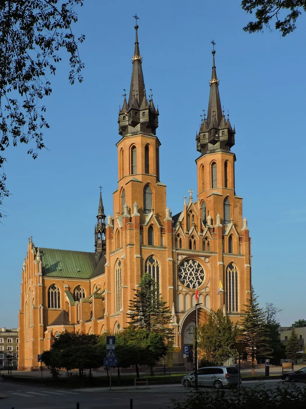 Neogotycka katedra w Radomiu z dwiema wysokimi wieżami i rozetowym oknem nad wejściem, w świetle zachodzącego słońca