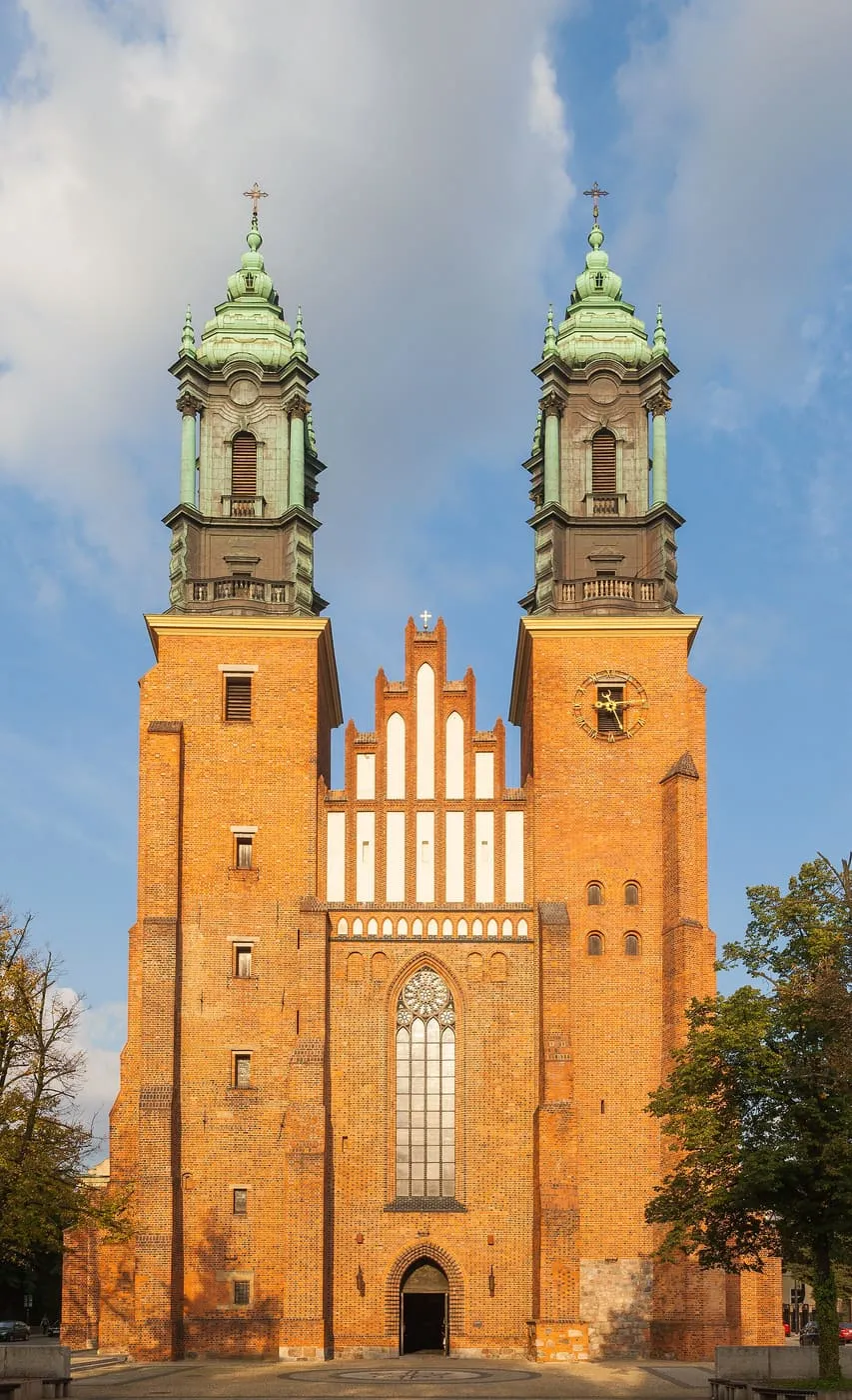Barokowa archikatedra poznańska z dwiema wieżami zwieńczonymi zielonymi kopułami, w złotym świetle zachodzącego słońca