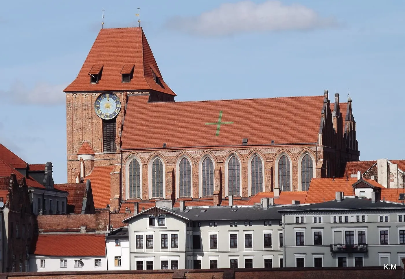 Ceglana katedra św. Janów w Toruniu z charakterystycznym zielonym krzyżem na dachu, widziana znad miejskich dachów