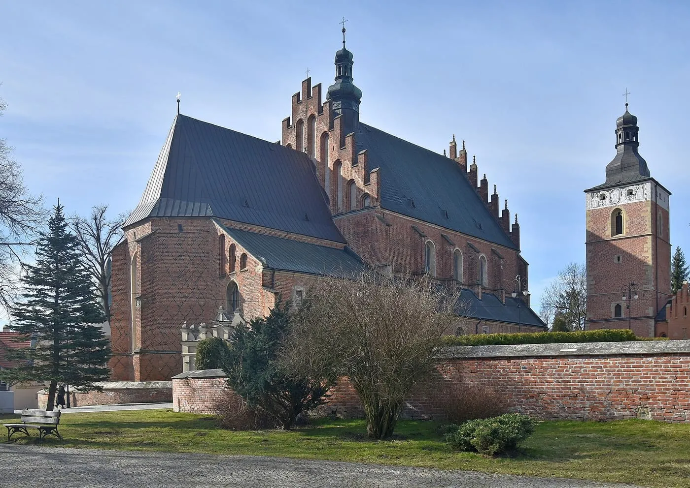 Późnogotycka, ceglana fara w Bieczu z wysokim dachem, schodkowym szczytem z sygnaturką i wzorem z ciemnej cegły na prezbiterium, obok ceglana dzwonnica z hełmem