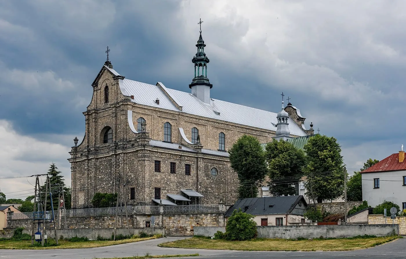 Neobarokowa kolegiata w Opocznie licowana szarym kamieniem, z wolutowym szczytem fasady i ażurową sygnaturką na dachu, na tle burzowych chmur