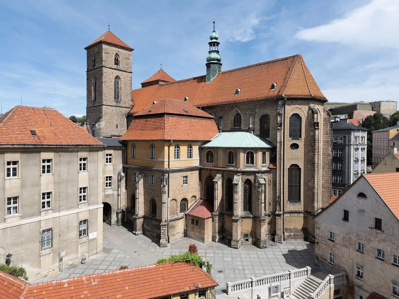 Gotycka kolegiata w Kłodzku widziana z góry, z kamienną wieżą i zieloną, barokową sygnaturką, otoczona czerwonymi dachami starówki