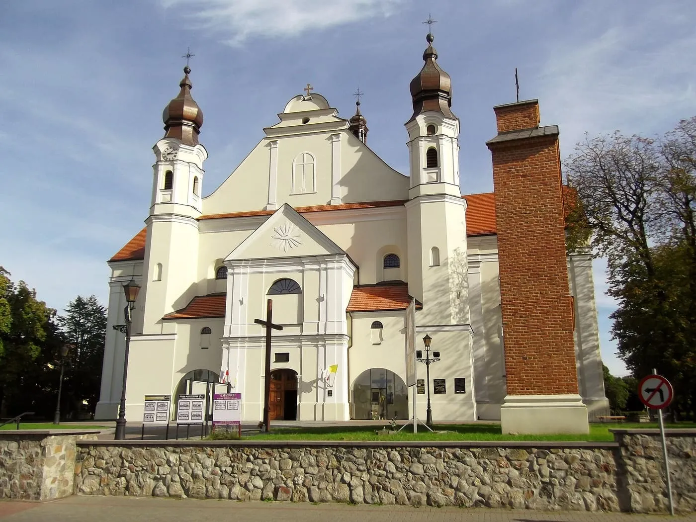 Biała kolegiata w Łasku z dwiema wieżami o cebulastych hełmach i wolnostojącą ceglaną dzwonnicą
