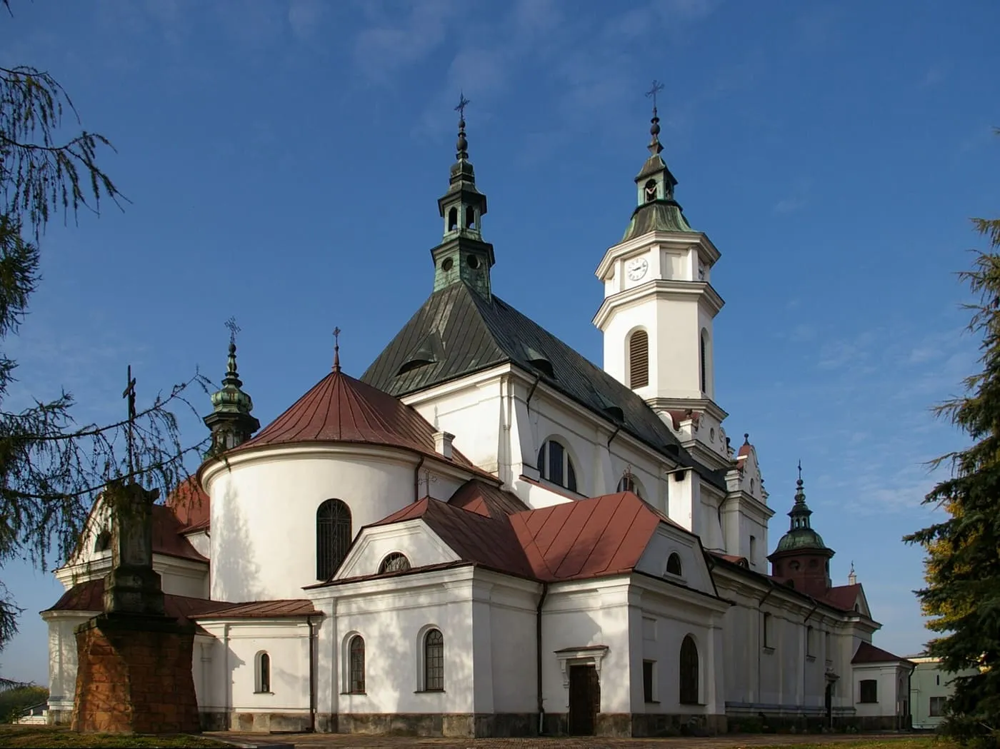 Biało-kremowa kolegiata św. Michała Archanioła w Ostrowcu Świętokrzyskim, z ciemnym, namiotowym dachem nad prezbiterium i kwadratową wieżą zegarową