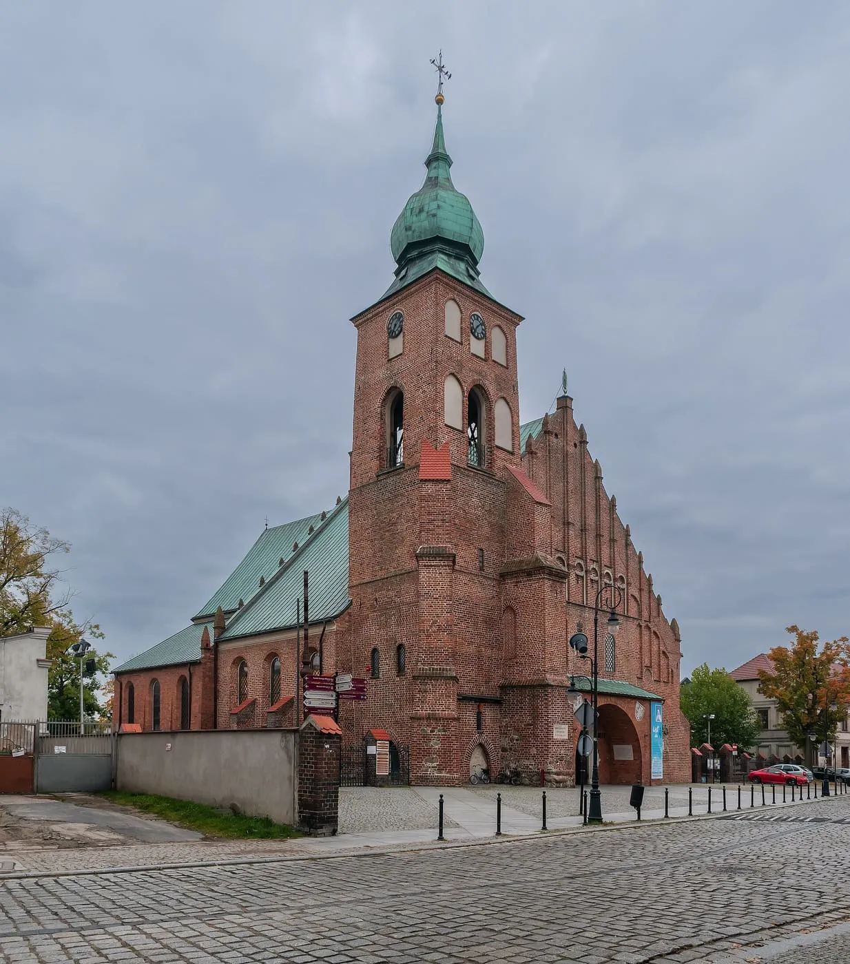 Ceglana wieża kolegiaty Wszystkich Świętych w Sieradzu z zieloną, cebulastą kopułą i iglicą, widziana znad rynku