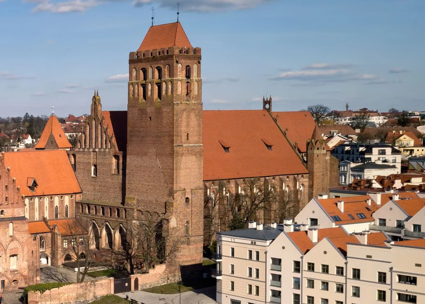 Widok z lotu ptaka na ceglaną wieżę konkatedry w Kwidzynie połączoną z murami zamku kapituły pomezańskiej, nad czerwonymi dachami miasta