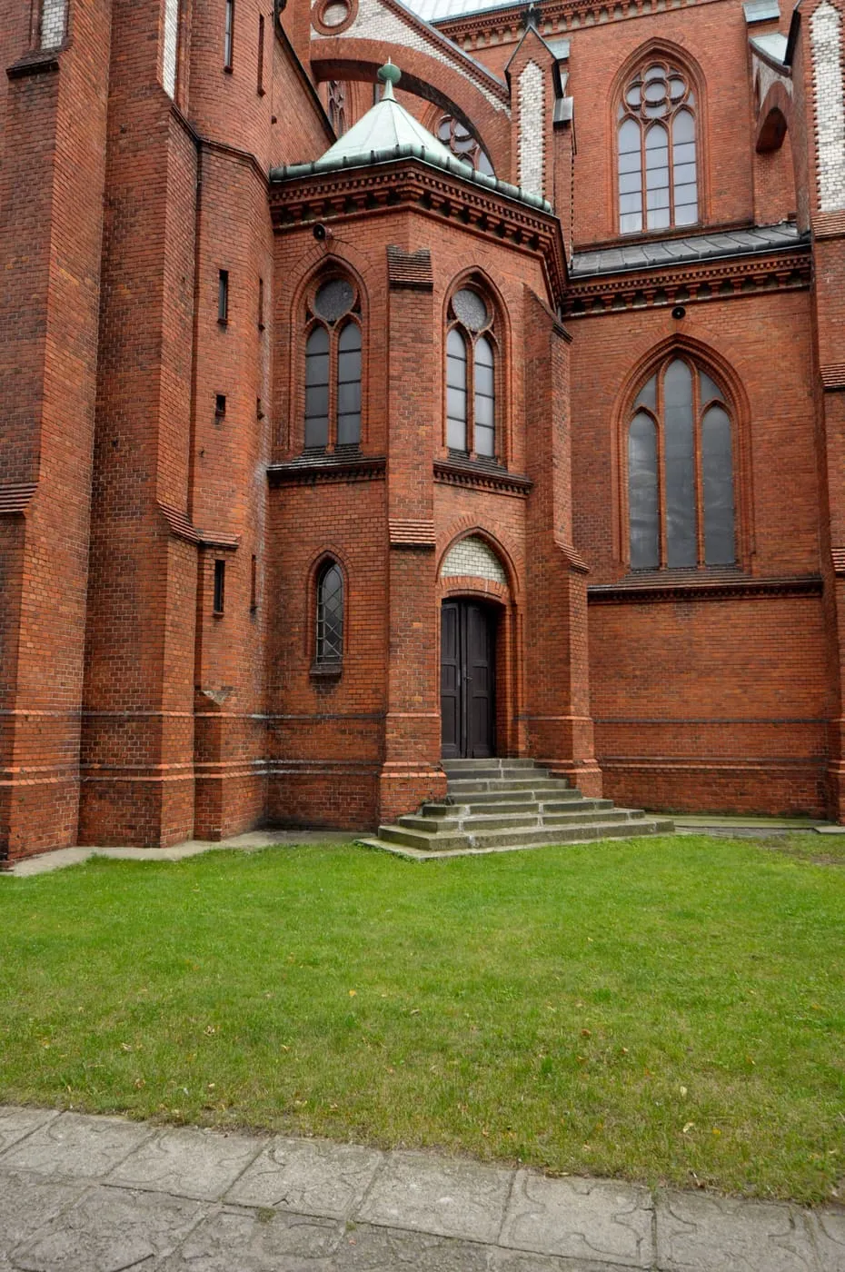 Ceglana, neogotycka apsyda kościoła Matki Bożej Pocieszenia w Żyrardowie z rozetowym oknem i wieżyczką zwieńczoną zieloną, spiczastą kopułką
