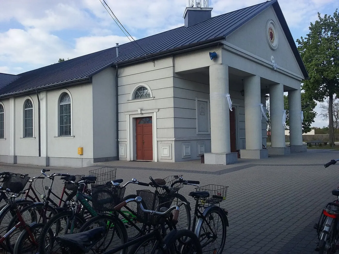 Klasycyzująca fasada kościoła Najświętszego Serca Jezusowego w Tomaszowie Mazowieckim z kolumnowym portykiem, okrągłym emblematem Najświętszego Serca i niewielką wieżyczką z krzyżem