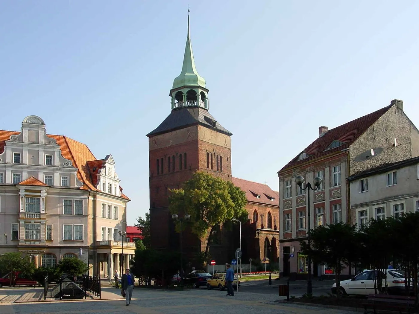 Ceglana wieża kościoła Narodzenia NMP w Białogardzie ze zwężającym się, miedzianym hełmem, widziana znad rynku pomiędzy kamienicami