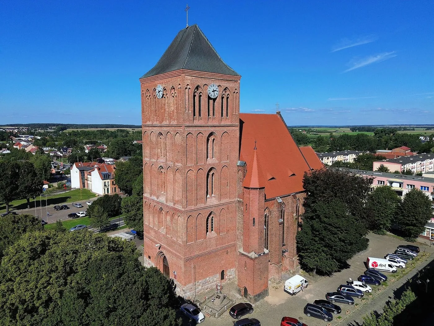 Ceglana, gotycka wieża kościoła Narodzenia NMP w Choszcznie z zegarami i blendami, nakryta ciemnym dachem namiotowym, obok nawa z czerwonym dachem, z lotu ptaka