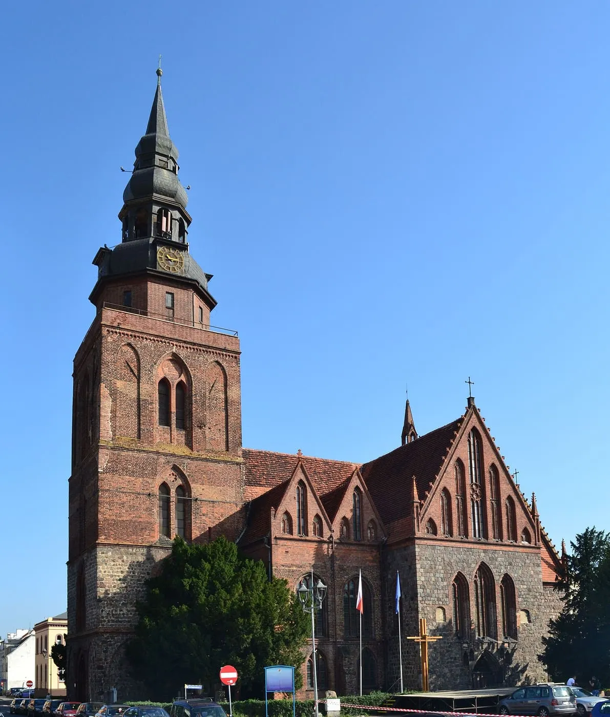Gotycki kościół Narodzenia NMP w Gryfinie z kamienno-ceglaną wieżą zwieńczoną ciemnym, barokowym hełmem z zegarem i szczytami z ostrołukowymi blendami, na tle błękitnego nieba