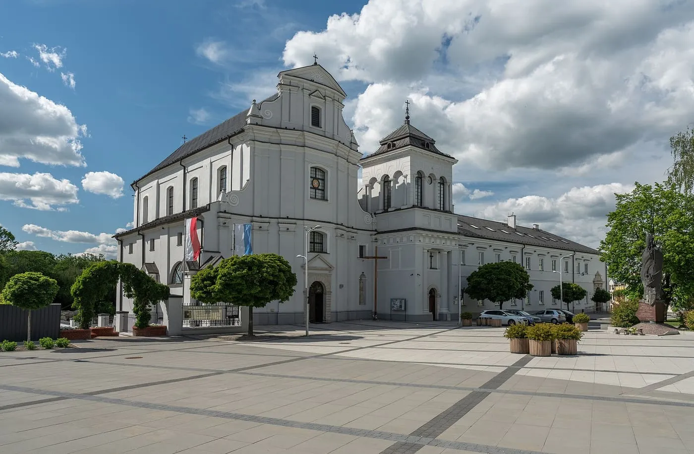 Biały, barokowy kościół w Rawie Mazowieckiej z falistym szczytem i osobno stojącą dzwonnicą, na tle błękitnego nieba