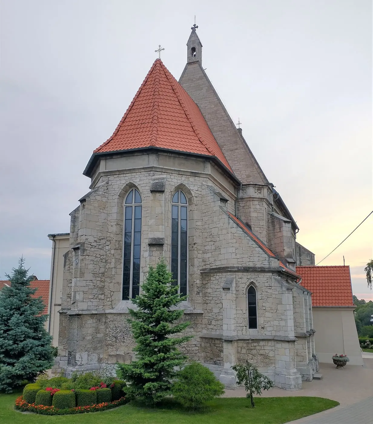 Kamienne, gotyckie prezbiterium kościoła w Stopnicy z wysokimi ostrołukowymi oknami, przyporami i czerwonym dachem, za nim szczyt nawy z kamienną sygnaturką