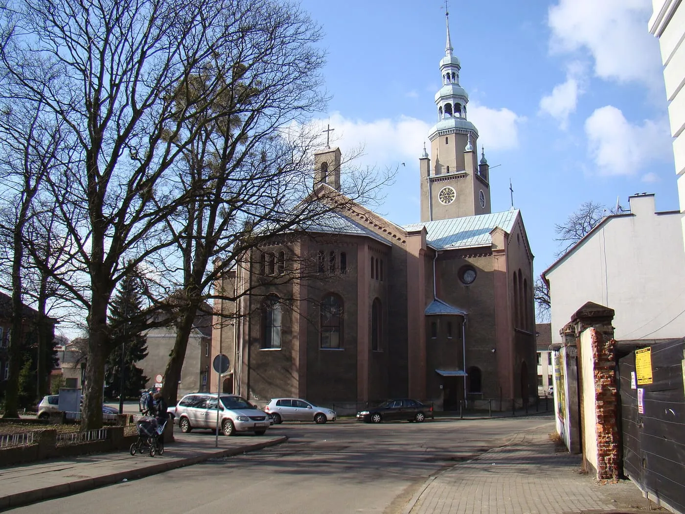Ceglana wieża kościoła Piotra i Pawła w Tarnowskich Górach z cynowym, spiczastym hełmem i zegarem, wśród bezlistnych drzew