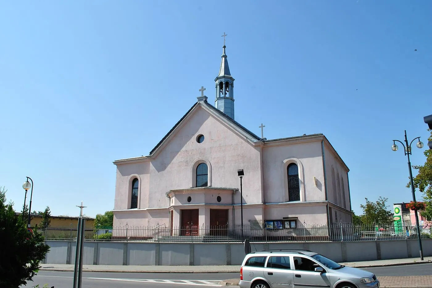 Biały, barokowy kościół z niewielką wieżyczką na sygnaturkę, za niskim murem przy ulicy
