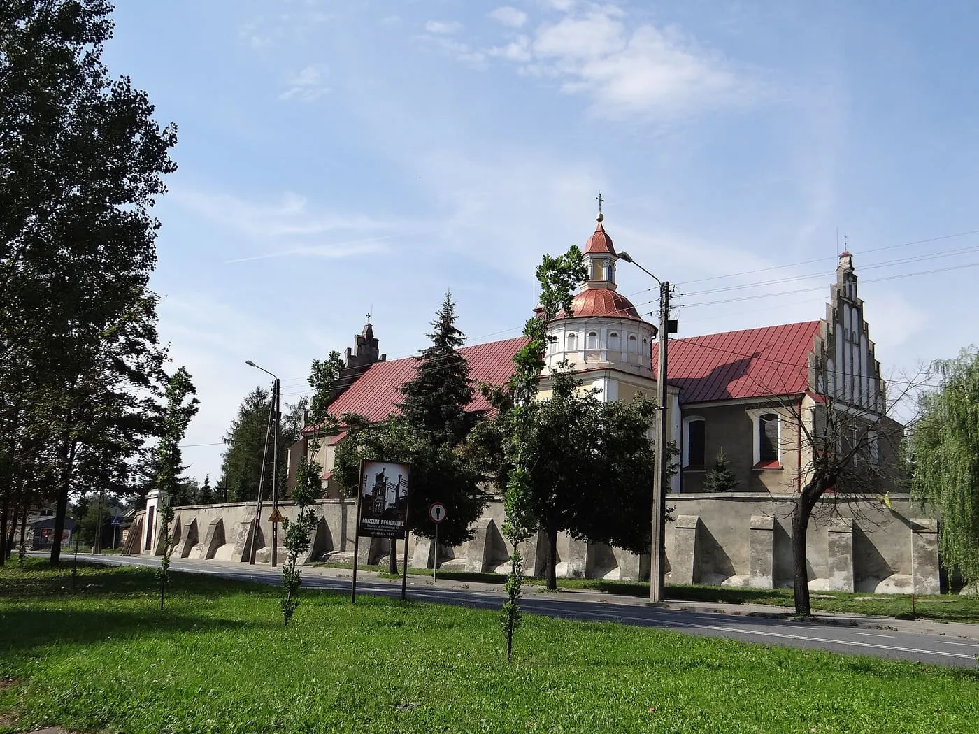 Kościół Podwyższenia Krzyża w Brzezinach z barokową wieżą zwieńczoną latarnią i gotyckim szczytem, za obronnym murem