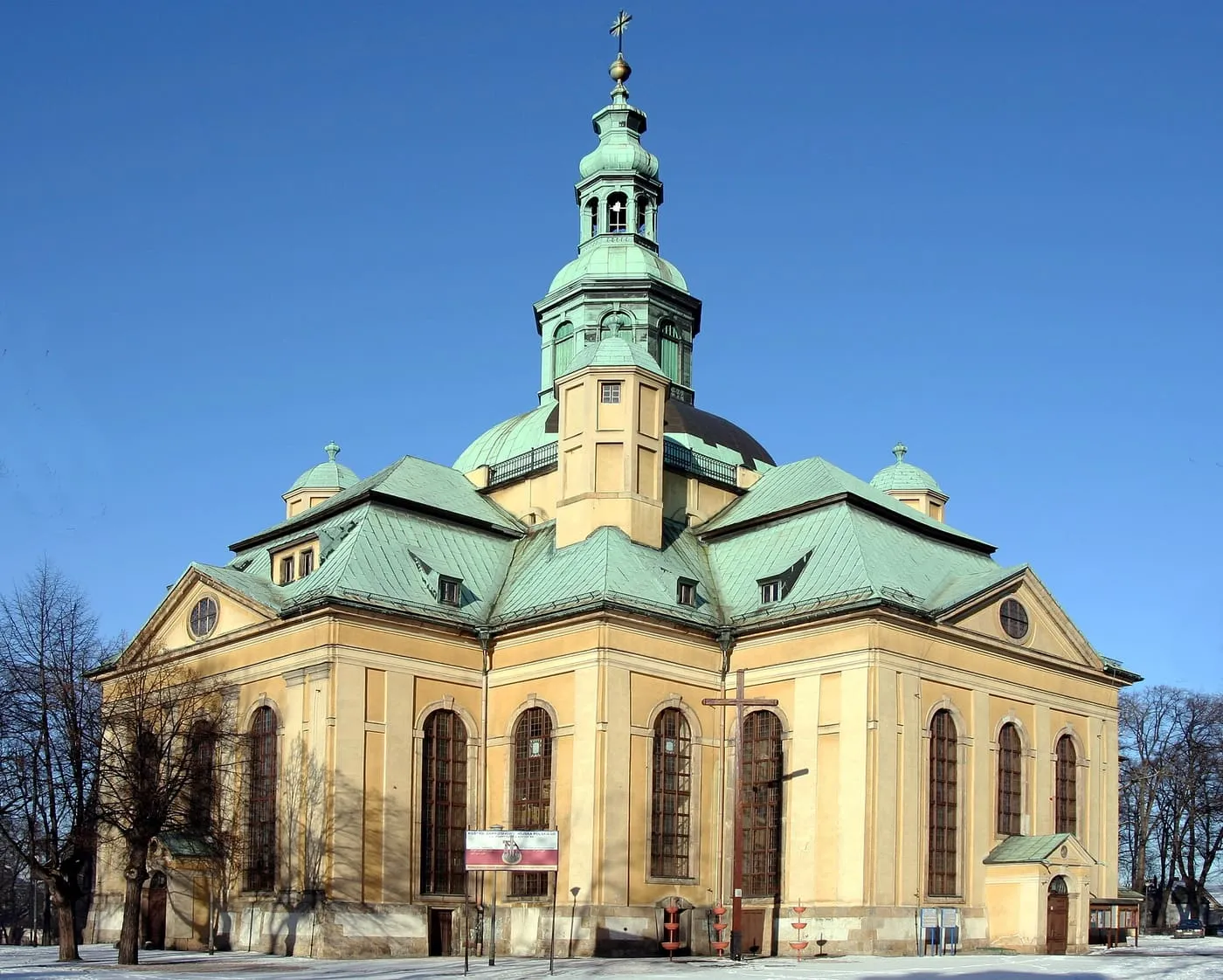 Żółta, barokowa fasada kościoła Podwyższenia Krzyża Świętego w Jeleniej Górze z zieloną kopułą i wieżyczką, zimą