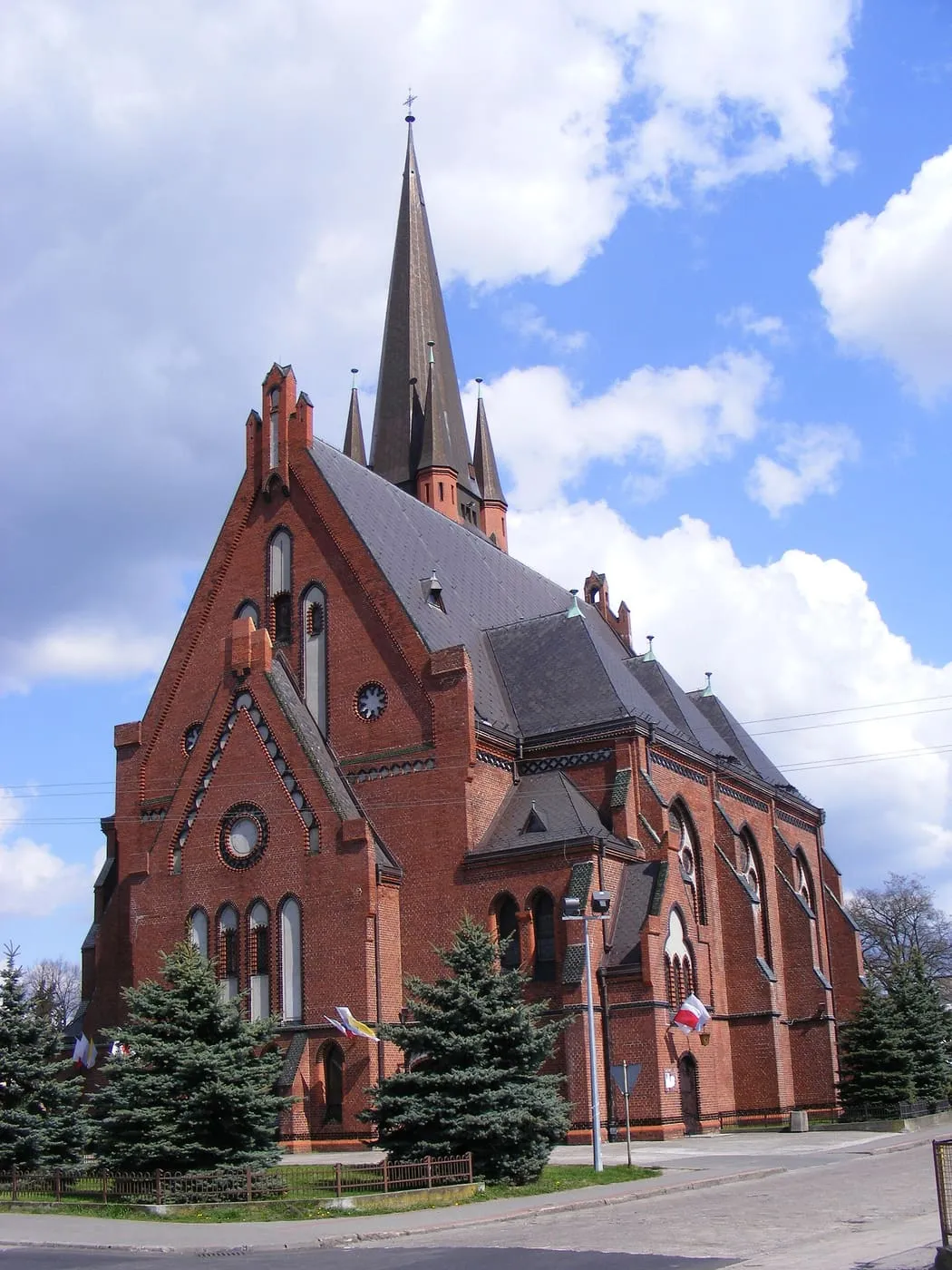 Neogotycki, ceglany kościół Przemienienia Pańskiego w Drezdenku ze schodkowymi szczytami, rozetami i wysoką, spiczastą iglicą wieży otoczoną narożnymi wieżyczkami