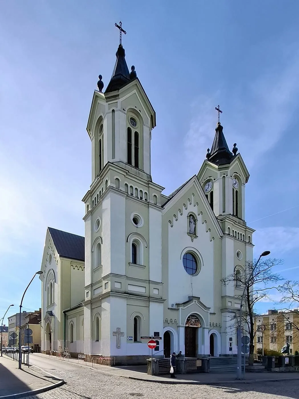Neoromańska, jasna fasada kościoła Przemienienia Pańskiego w Sanoku z dwiema wieżami zegarowymi i oknem rozetowym