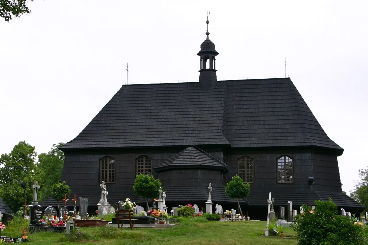 Czarny, drewniany kościół cmentarny św. Anny w Czarnowąsach, otoczony nagrobkami