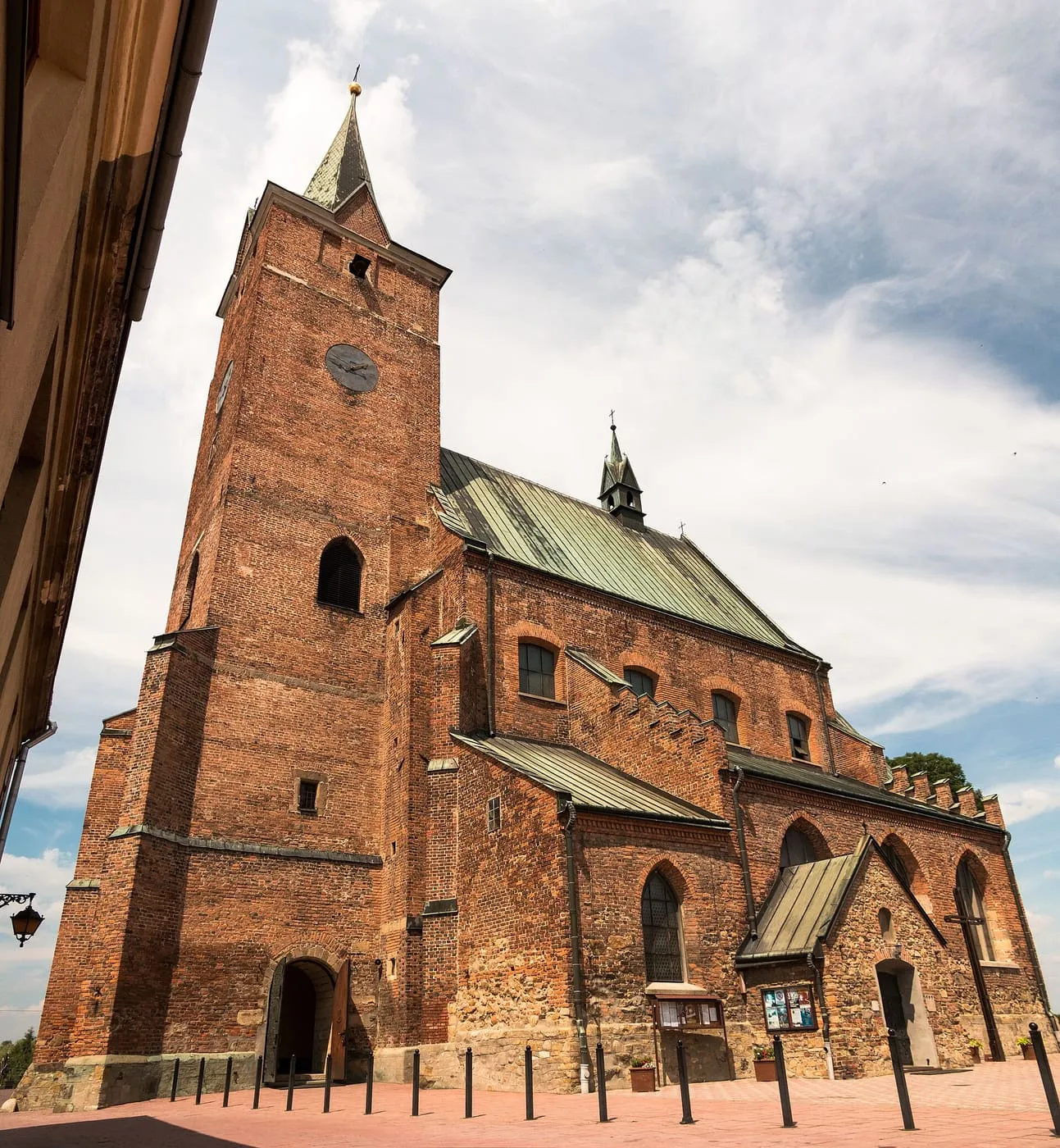 Gotycka, ceglana fara w Pilźnie z wysoką czworoboczną wieżą z zegarem i spiczastym hełmem, miedzianymi dachami i sygnaturką, widziana od strony placu z żabiej perspektywy