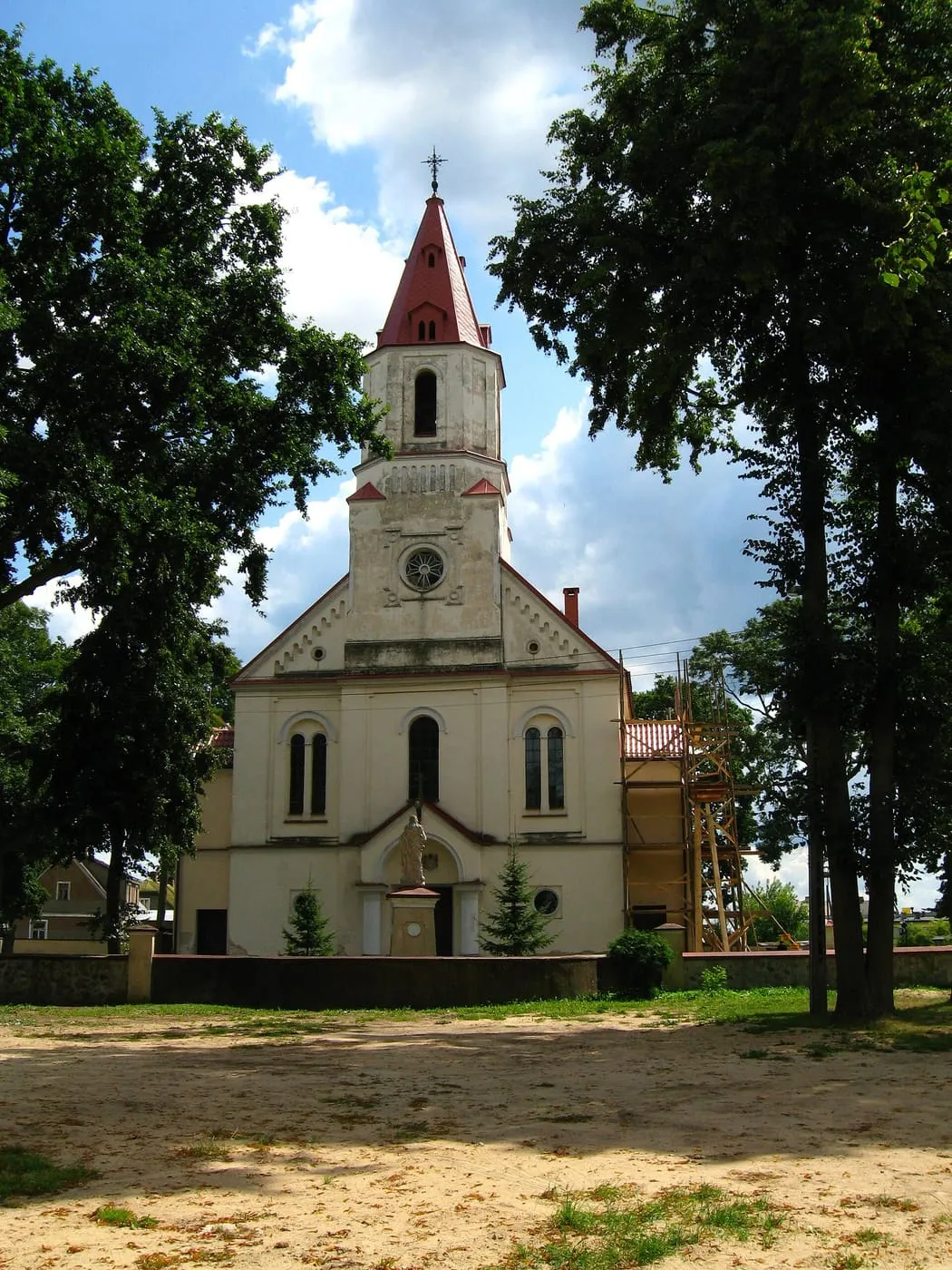 Biała wieża kościoła św. Jana w Knyszynie z czerwoną, spiczastą iglicą i narożnymi wieżyczkami, wśród drzew